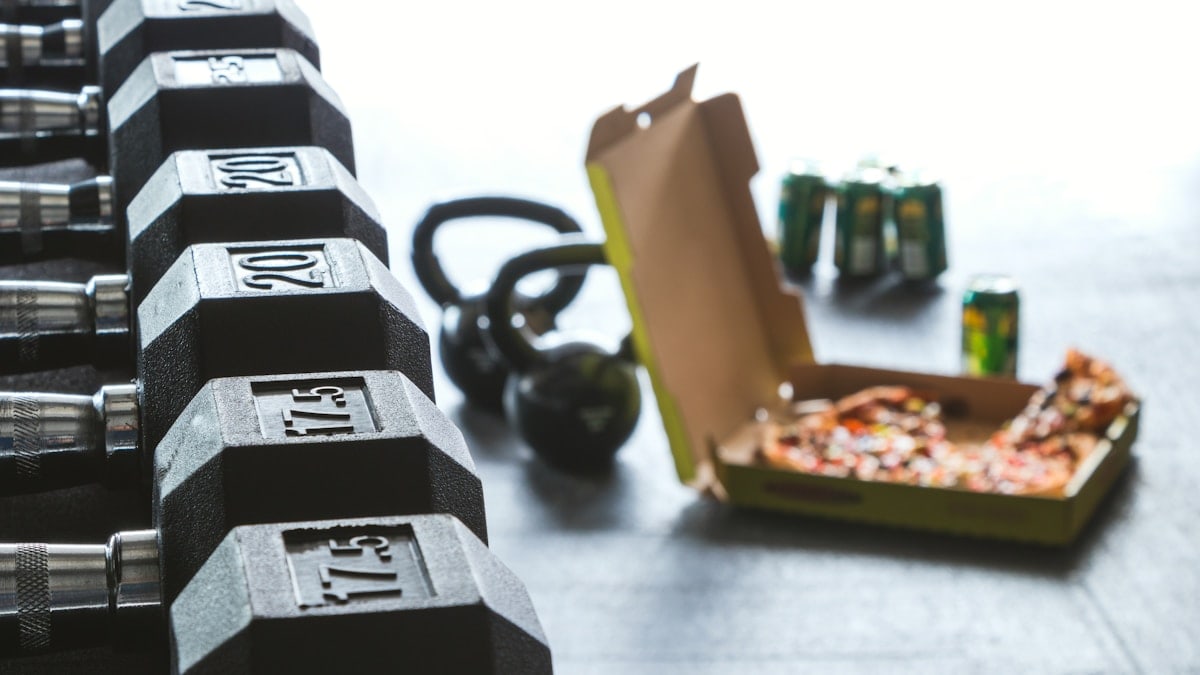 dumbbell weights in focus with beer and pizza off to one side soft focus