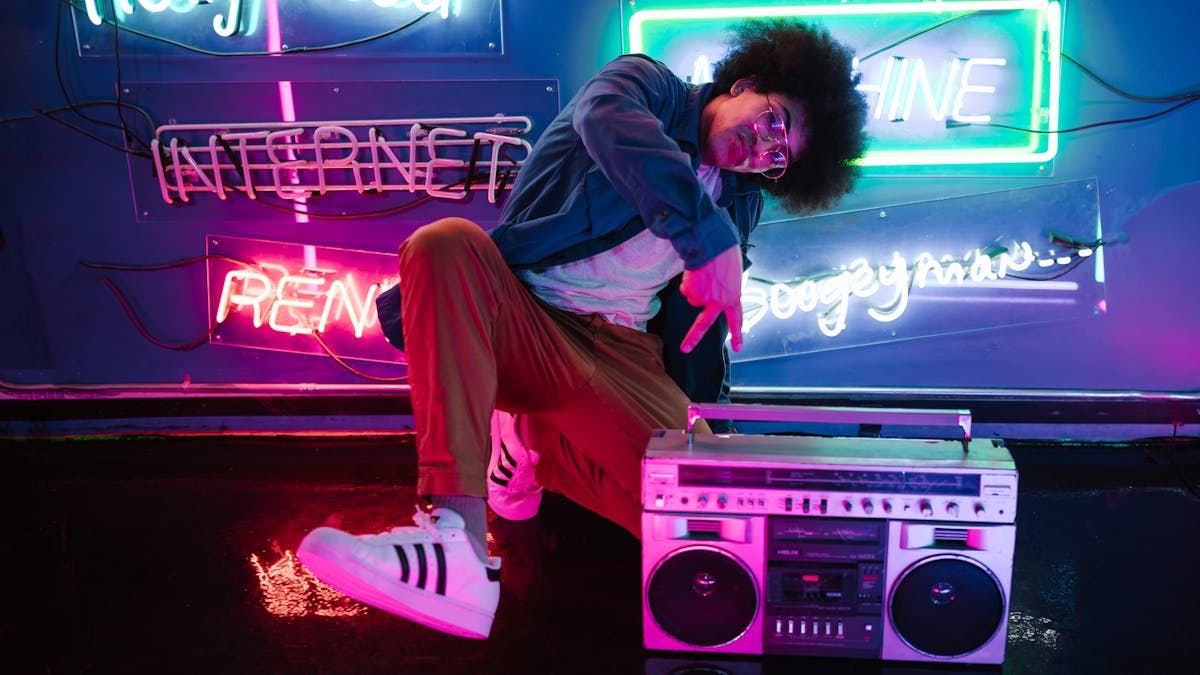 Stylish man poses with a retro boombox in a vibrant neon-lit club scene, evoking a cool nightlife vibe.